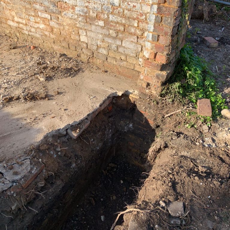 Section 6 party wall notice Excavated area near brick wall, showing a deep trench beside a house foundation.