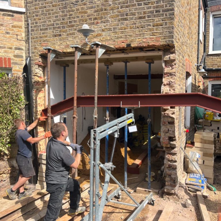 Party wall section 3 and 6 Men supporting a steel beam during home renovation, with construction materials around.
