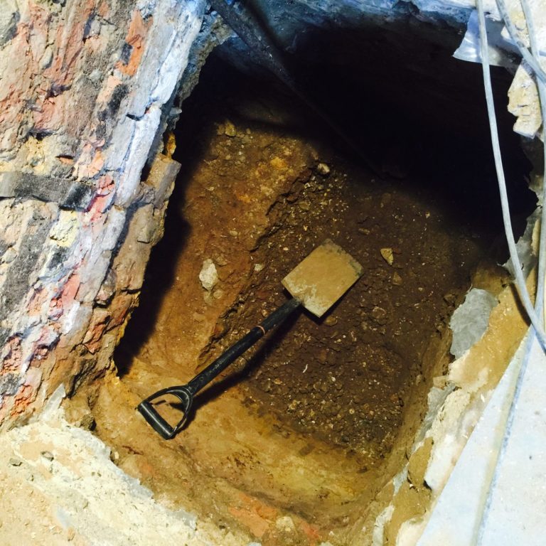 Underpinning party wall An excavation hole for underpinning a party wall with a shovel resting in the dirt.